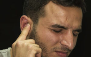 man putting finger to ear with pained expression