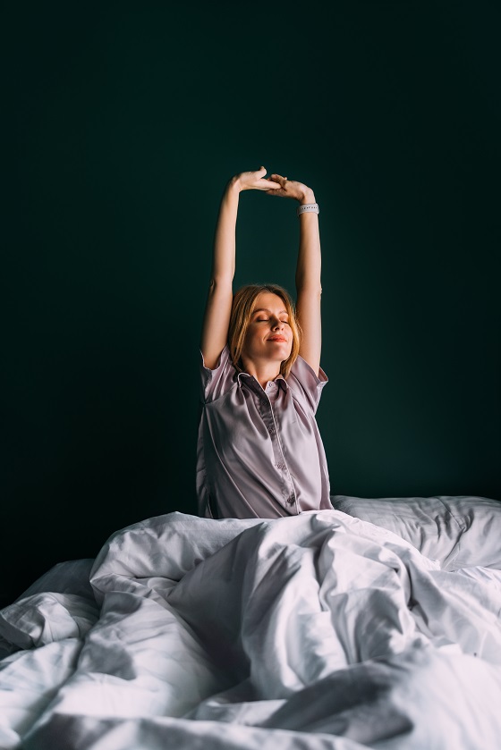 A charming Caucasian female in bed smiling while getting up.